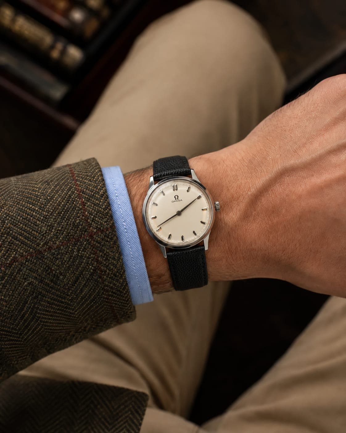 A vintage Omega on a black leather strap, worn with a tweed jacket